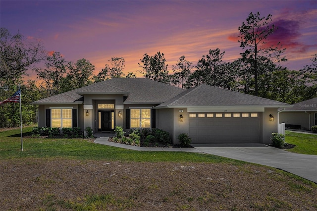 prairie-style home with a shingled roof, an attached garage, stucco siding, a front lawn, and driveway