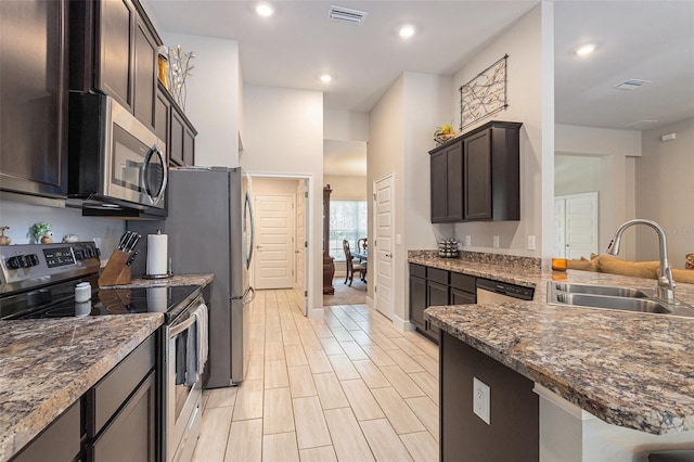 kitchen with visible vents, a sink, appliances with stainless steel finishes, dark brown cabinetry, and dark stone counters