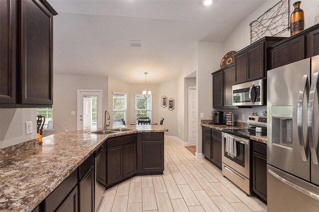 kitchen with a sink, a peninsula, dark brown cabinets, stainless steel appliances, and stone countertops