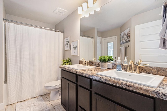 full bath featuring toilet, double vanity, a sink, and visible vents