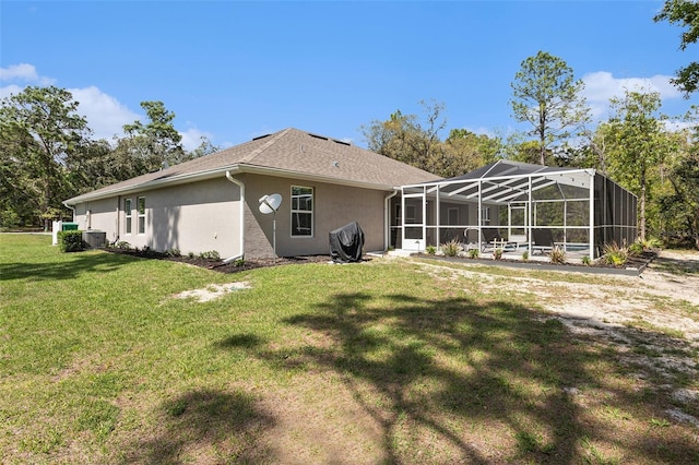 rear view of house with a yard, a lanai, and stucco siding
