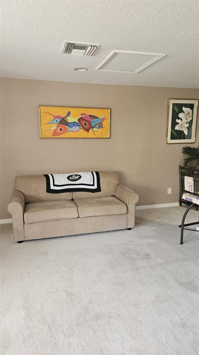 living area featuring attic access, a textured ceiling, baseboards, visible vents, and carpet