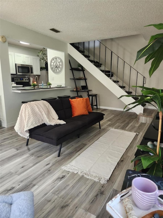 living room featuring stairs, visible vents, a textured ceiling, and wood finished floors