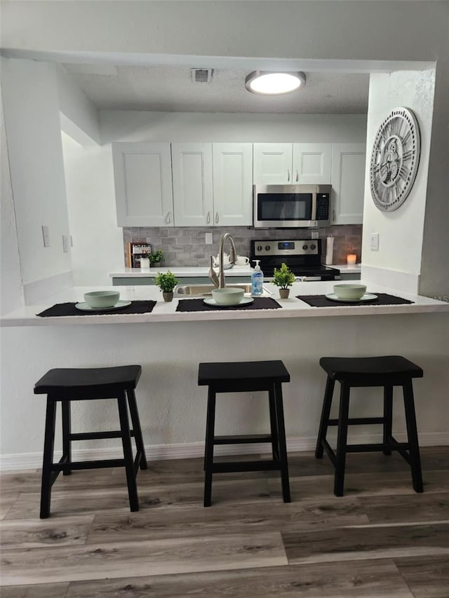 kitchen with stainless steel appliances, dark wood-type flooring, a breakfast bar area, and decorative backsplash