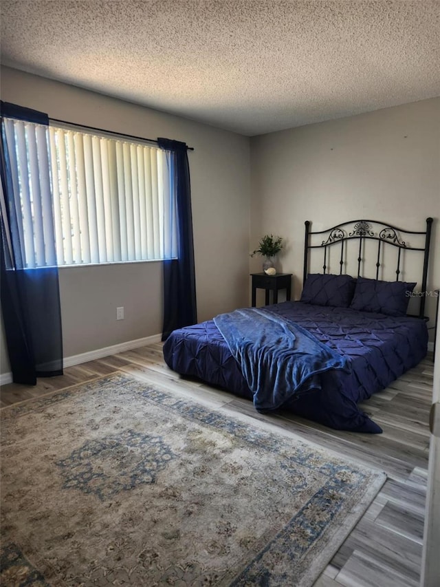 bedroom with a textured ceiling, wood finished floors, and baseboards