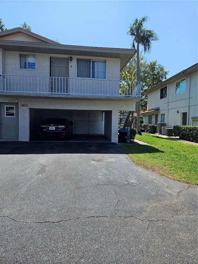 view of front of property featuring a carport, stucco siding, a front lawn, aphalt driveway, and central AC