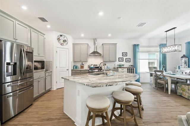 kitchen featuring stainless steel appliances, gray cabinetry, visible vents, and wall chimney range hood