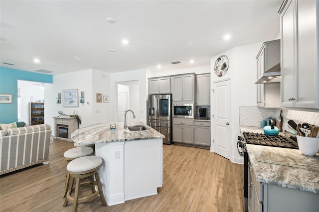 kitchen with a sink, light wood-style floors, stainless steel appliances, gray cabinets, and decorative backsplash