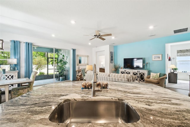 kitchen with stone countertops, open floor plan, a ceiling fan, visible vents, and a sink