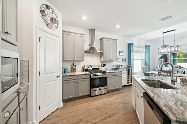 kitchen featuring wall chimney exhaust hood, visible vents, gray cabinets, appliances with stainless steel finishes, and a sink