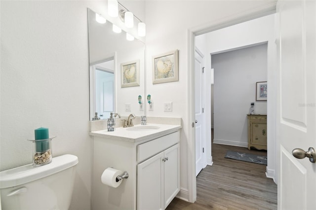 bathroom featuring toilet, vanity, wood finished floors, and baseboards