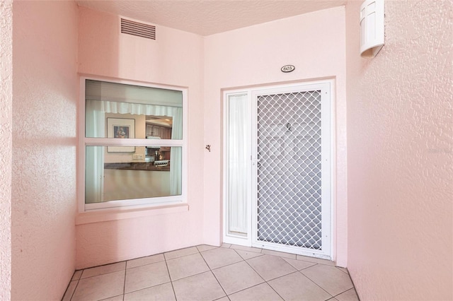 exterior space with a textured wall, visible vents, and light tile patterned flooring