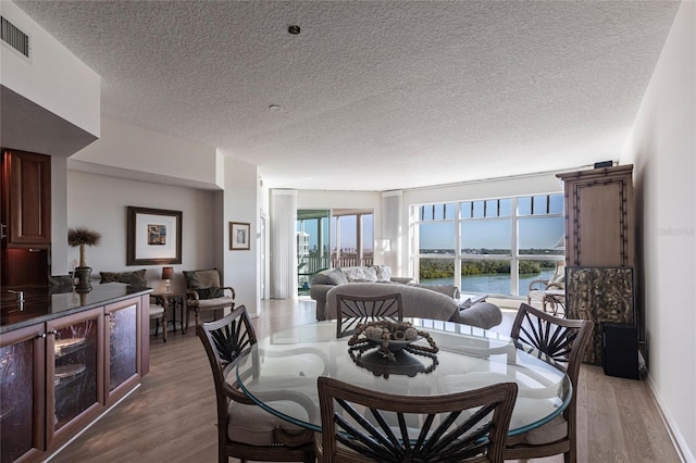 dining area with a water view, visible vents, a textured ceiling, and wood finished floors