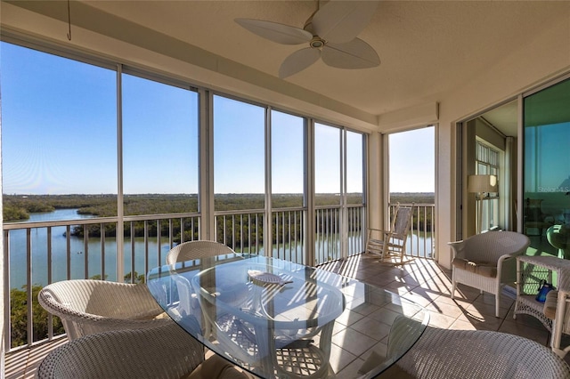 sunroom / solarium featuring a water view, tile patterned floors, and ceiling fan