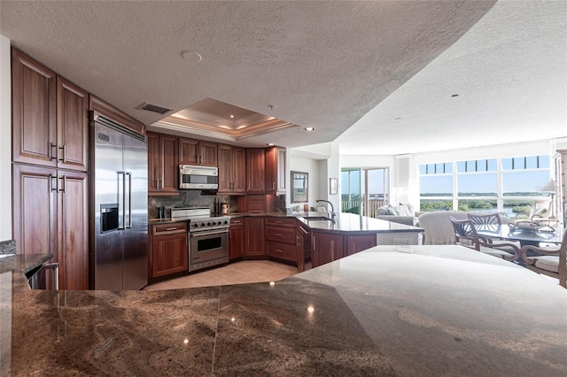 kitchen with high quality appliances, a peninsula, a textured ceiling, visible vents, and a sink