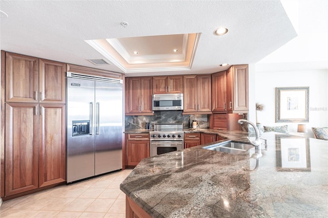 kitchen featuring visible vents, brown cabinetry, decorative backsplash, premium appliances, and a sink