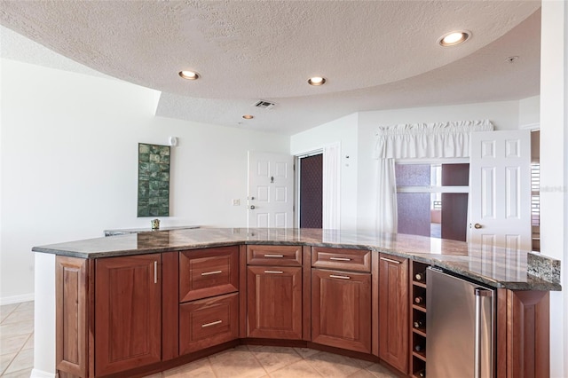 kitchen featuring dark stone counters, light tile patterned floors, refrigerator, visible vents, and recessed lighting