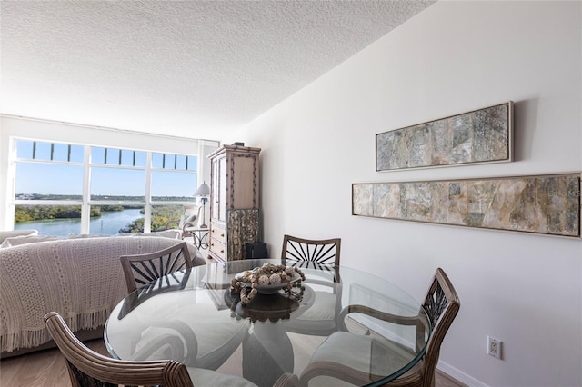 dining room with a textured ceiling, wood finished floors, baseboards, and a water view