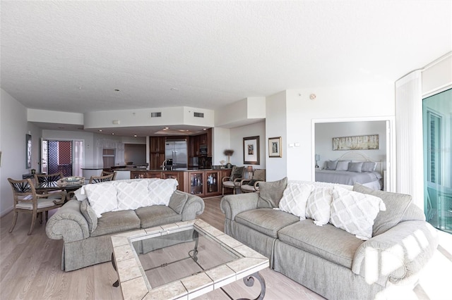 living area featuring a textured ceiling, light wood finished floors, and visible vents