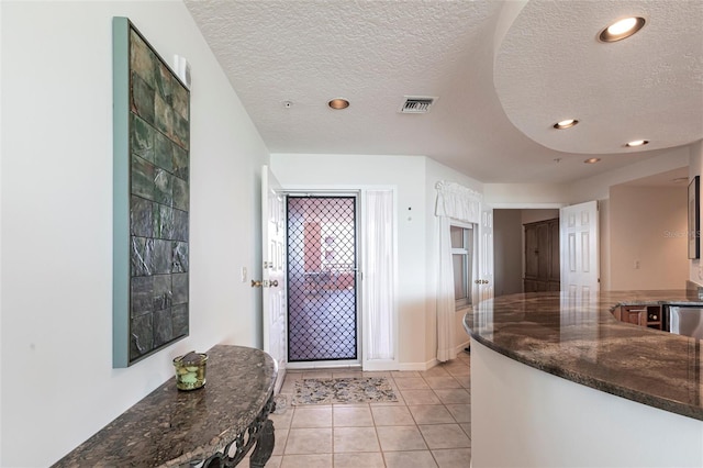 foyer with visible vents, baseboards, light tile patterned floors, and a textured ceiling