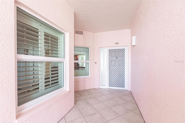 interior space featuring visible vents, light tile patterned floors, a textured wall, and a textured ceiling
