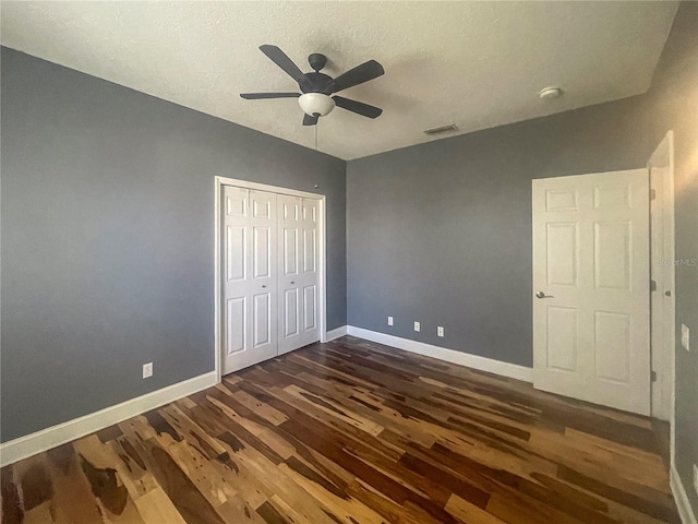 unfurnished bedroom with a closet, dark wood-style flooring, baseboards, visible vents, and a ceiling fan