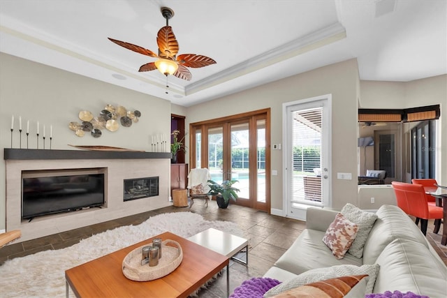 5807 Thoreau Pl, Lithia, FL 33547 - living room featuring a raised ceiling, ornamental molding, a ceiling fan, stone tile flooring, and a fireplace