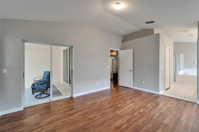 11626 Pure Pebble Dr, Riverview, FL 33569 - unfurnished bedroom with vaulted ceiling, wood finished floors, baseboards, ensuite bathroom, and arched walkways