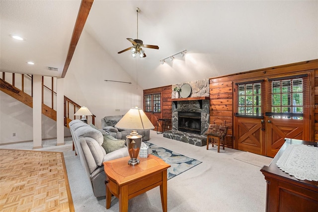 living area with light colored carpet, a ceiling fan, a stone fireplace, vaulted ceiling, and visible vents