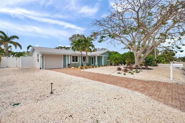 single story home featuring a garage, gravel driveway, fence, and a gate
