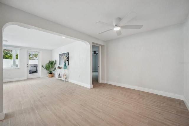 unfurnished room with arched walkways, light wood-style floors, baseboards, and a ceiling fan