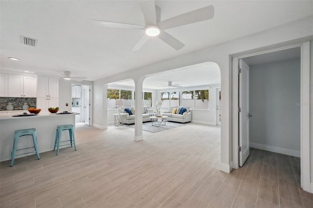 living area featuring visible vents, baseboards, arched walkways, ceiling fan, and light wood-style floors