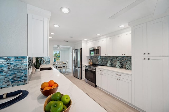 kitchen with tasteful backsplash, white cabinetry, stainless steel appliances, arched walkways, and a sink