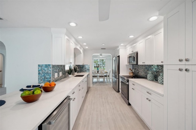 kitchen featuring arched walkways, a sink, a ceiling fan, white cabinetry, and stainless steel appliances