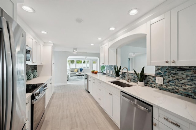 kitchen with arched walkways, a sink, ceiling fan, white cabinetry, and stainless steel appliances
