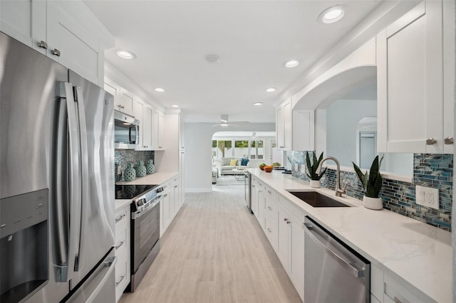 kitchen with a ceiling fan, white cabinets, light stone countertops, stainless steel appliances, and a sink