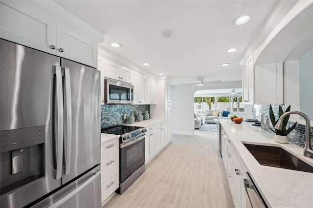 kitchen with tasteful backsplash, open floor plan, white cabinets, appliances with stainless steel finishes, and a sink