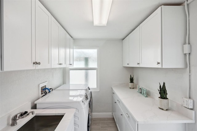 clothes washing area featuring light wood-style floors, independent washer and dryer, a sink, baseboards, and cabinet space