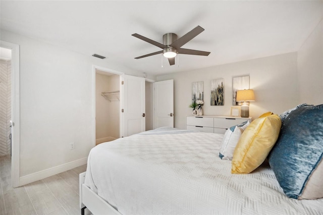 bedroom with ceiling fan, light wood-type flooring, a spacious closet, visible vents, and baseboards