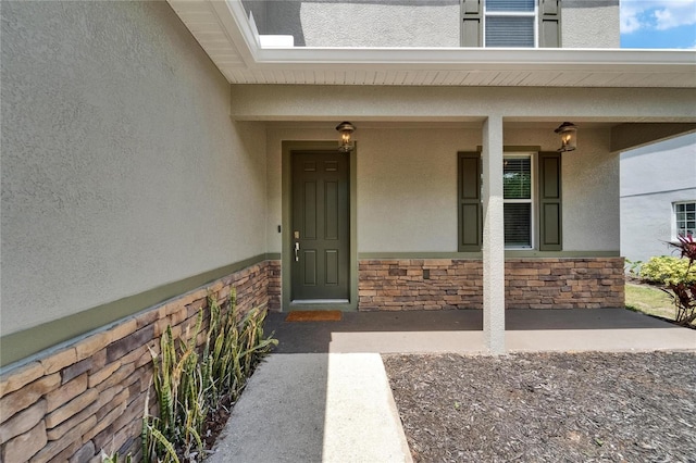 entrance to property with covered porch, stucco siding, and stone siding