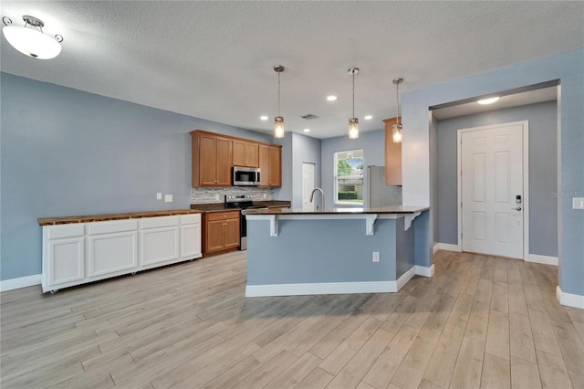 kitchen with a peninsula, light wood-style floors, a kitchen bar, stainless steel appliances, and a sink