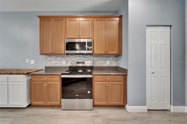kitchen with baseboards, dark countertops, appliances with stainless steel finishes, light wood-style floors, and backsplash