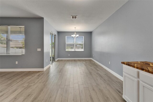 unfurnished dining area with baseboards, a chandelier, a textured ceiling, visible vents, and light wood finished floors