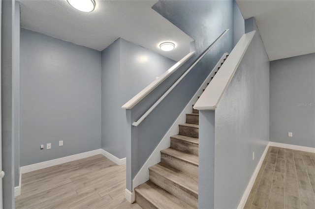 staircase with baseboards, a textured ceiling, and wood finished floors