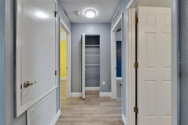 hall with light wood-type flooring, baseboards, visible vents, and a textured ceiling