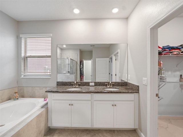 full bathroom with a sink, a walk in closet, a stall shower, and a garden tub
