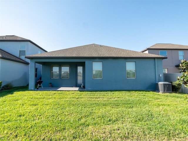 rear view of house with roof with shingles, stucco siding, central AC unit, a patio area, and a yard