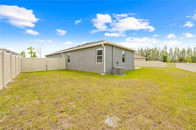 rear view of house featuring stucco siding, a fenced backyard, central AC, a gate, and a lawn