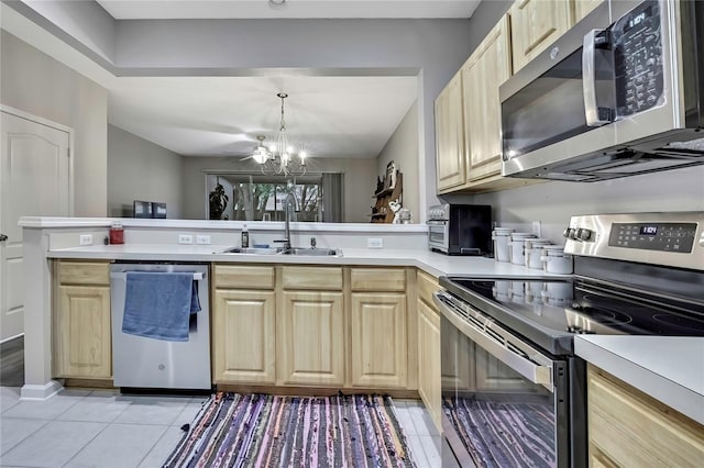 kitchen with a peninsula, light tile patterned flooring, stainless steel appliances, a sink, and light brown cabinetry