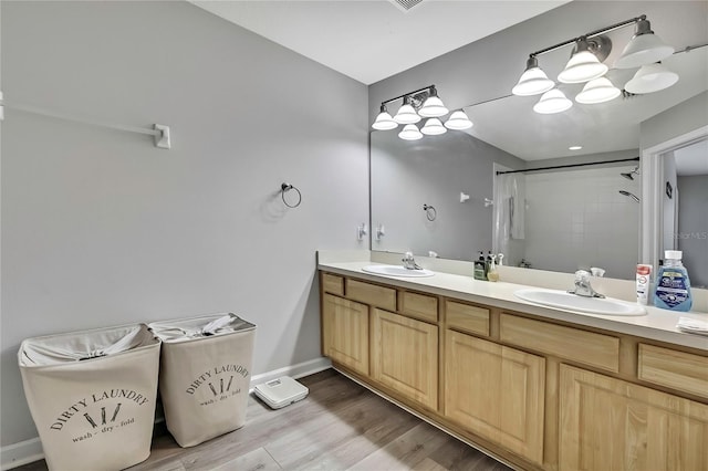 bathroom with a shower, wood finished floors, double vanity, and a sink